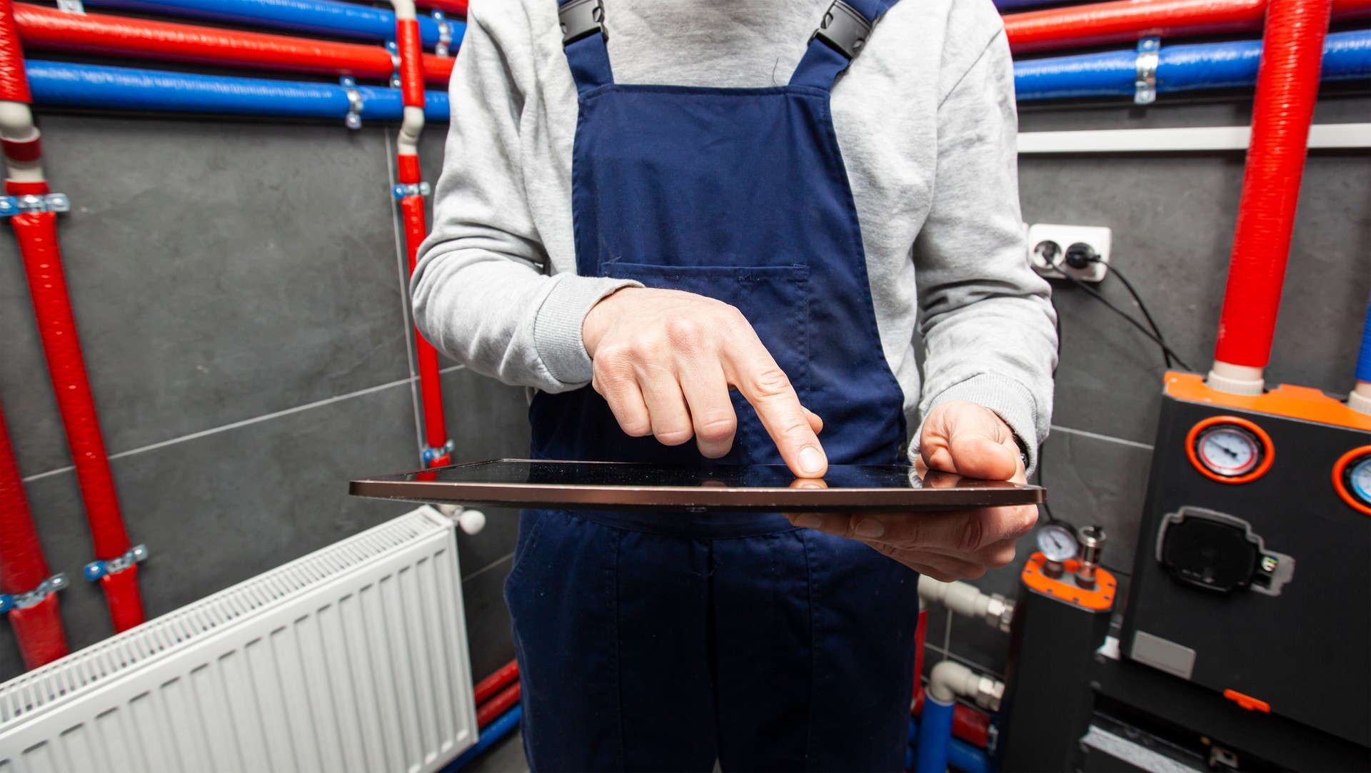 Der Techniker, der die Heizungsanlage im Heizraum mit Tablet in der Hand überprüft